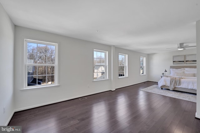 unfurnished bedroom featuring multiple windows, dark wood finished floors, and baseboards