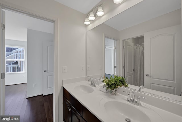 bathroom with double vanity, wood finished floors, a sink, and baseboards