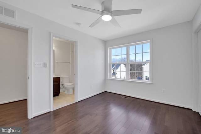 unfurnished bedroom featuring dark wood-type flooring, ensuite bath, visible vents, and baseboards