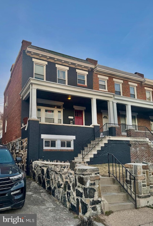 view of property with a porch, brick siding, and stairway