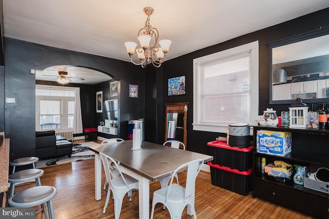 dining area featuring ceiling fan with notable chandelier, arched walkways, and wood finished floors