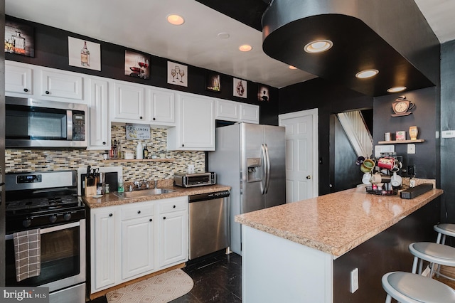 kitchen with decorative backsplash, white cabinets, appliances with stainless steel finishes, a breakfast bar area, and a sink