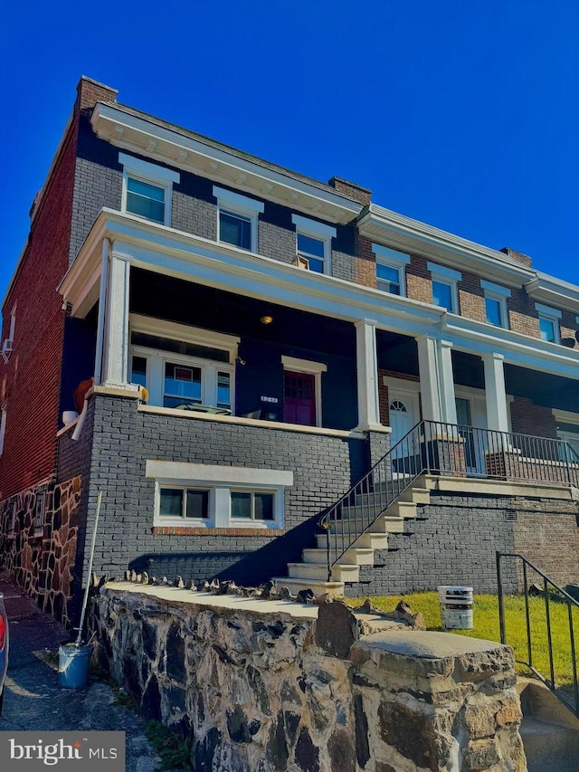 view of front facade featuring covered porch, stairs, and brick siding