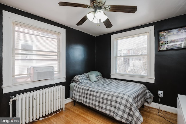 bedroom with cooling unit, a ceiling fan, baseboards, radiator, and light wood finished floors