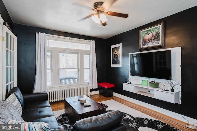 living room with radiator, a ceiling fan, baseboards, and wood finished floors