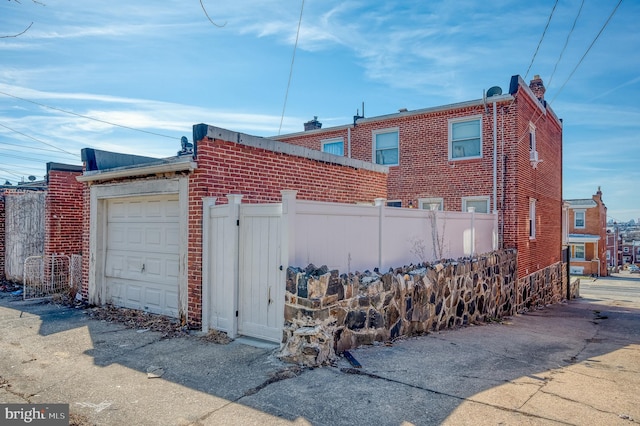 view of property exterior featuring brick siding, a detached garage, and fence