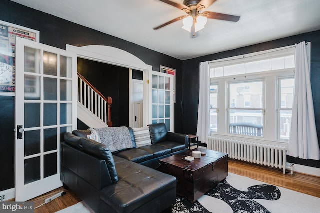 living area with radiator, ceiling fan, stairway, and wood finished floors