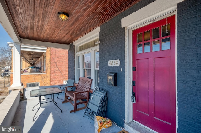 view of exterior entry with brick siding and a porch