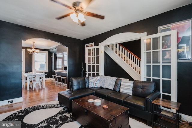 living room with arched walkways, stairway, wood finished floors, baseboards, and ceiling fan with notable chandelier