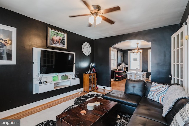 living area with baseboards, arched walkways, wood finished floors, and ceiling fan with notable chandelier