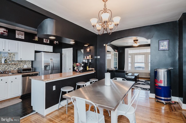 kitchen featuring stainless steel appliances, arched walkways, white cabinets, and hanging light fixtures