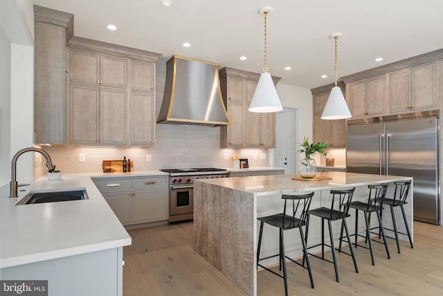 kitchen with a kitchen island, a sink, high end appliances, light wood-style flooring, and wall chimney exhaust hood
