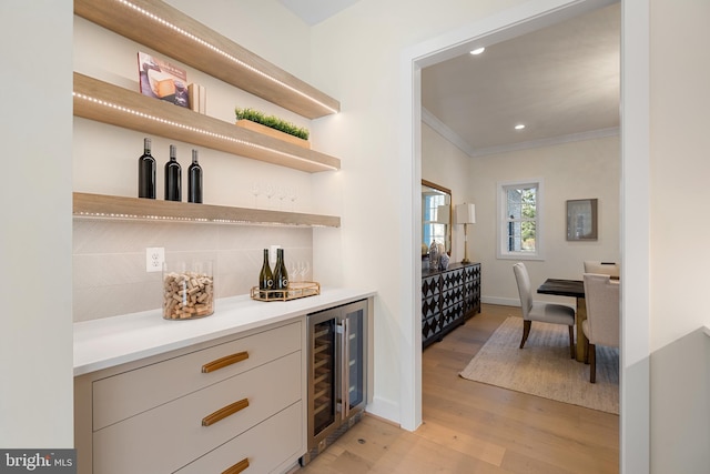 bar with a bar, ornamental molding, tasteful backsplash, light wood-type flooring, and beverage cooler