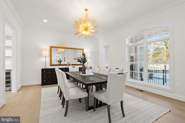 dining space featuring baseboards, light wood-type flooring, crown molding, and an inviting chandelier