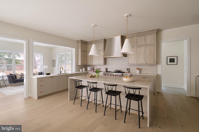 kitchen featuring light countertops, light wood-style flooring, a kitchen bar, wall chimney range hood, and backsplash