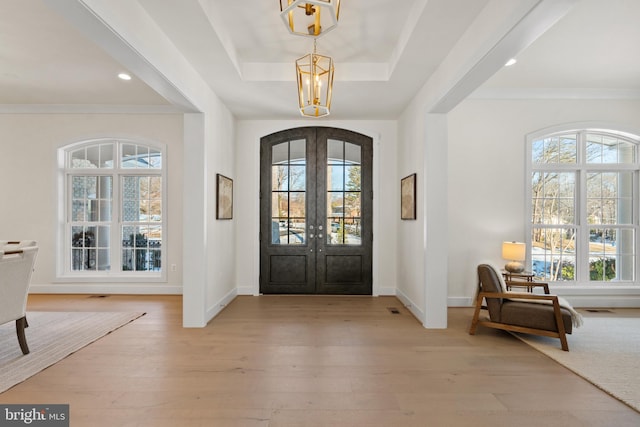 entryway featuring light wood-type flooring, french doors, plenty of natural light, a raised ceiling, and a notable chandelier