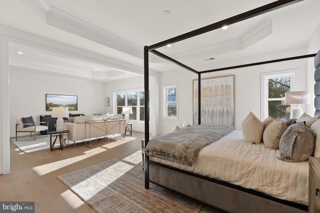 bedroom with a raised ceiling, ornamental molding, multiple windows, and wood finished floors