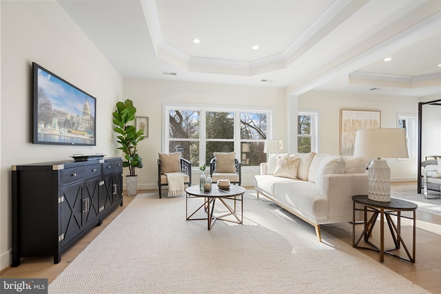 living area with visible vents, crown molding, light wood-type flooring, and a raised ceiling