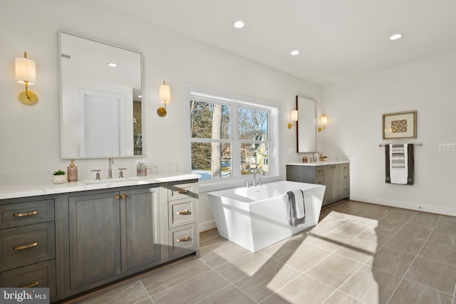 full bath featuring a sink, a freestanding tub, recessed lighting, and two vanities