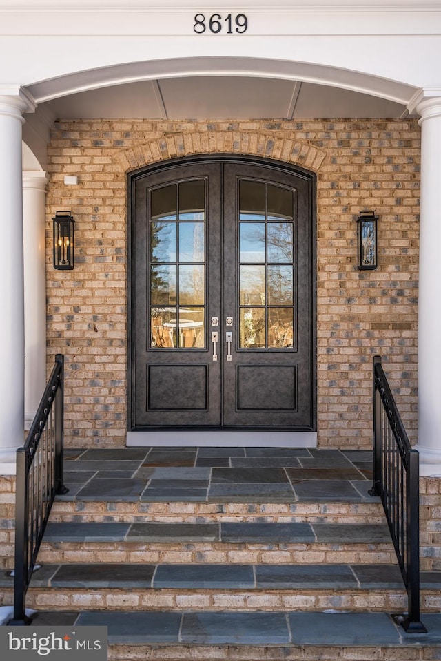 view of exterior entry with brick siding, covered porch, and french doors