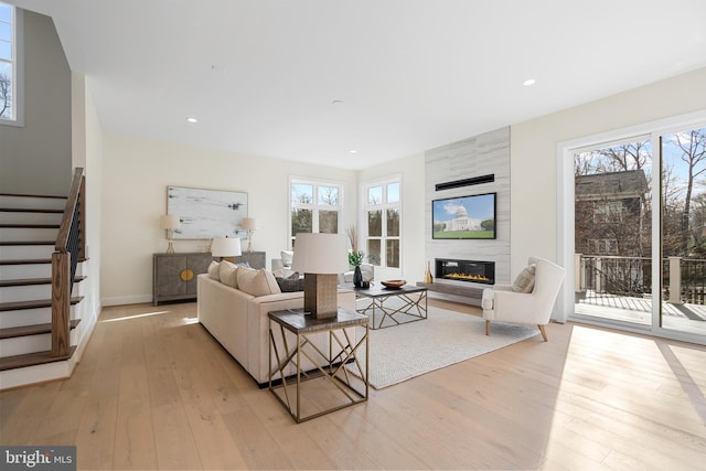 living area with stairs, recessed lighting, light wood-style floors, and a large fireplace