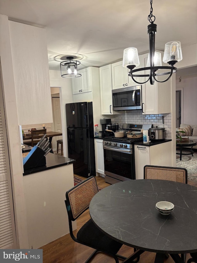 kitchen featuring a chandelier, dark countertops, appliances with stainless steel finishes, white cabinetry, and pendant lighting