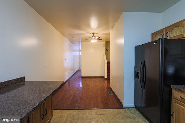 kitchen featuring dark wood-type flooring, black refrigerator with ice dispenser, dark stone counters, and ceiling fan