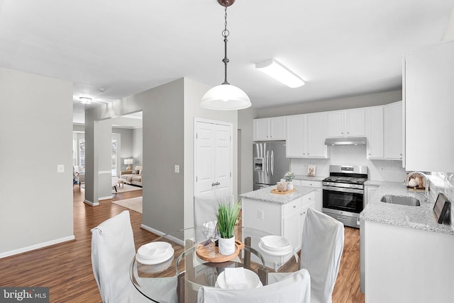 kitchen with sink, white cabinetry, stainless steel appliances, light stone counters, and decorative light fixtures