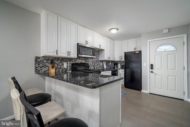 kitchen with a breakfast bar area, tasteful backsplash, black appliances, white cabinets, and kitchen peninsula