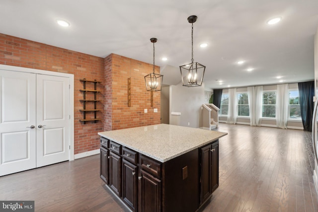 kitchen featuring a center island, dark brown cabinets, hanging light fixtures, dark hardwood / wood-style floors, and brick wall