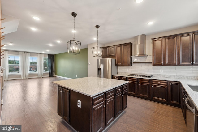 kitchen featuring a kitchen island, pendant lighting, stainless steel appliances, dark brown cabinets, and wall chimney exhaust hood