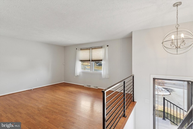 interior space with a textured ceiling, visible vents, a notable chandelier, and wood finished floors