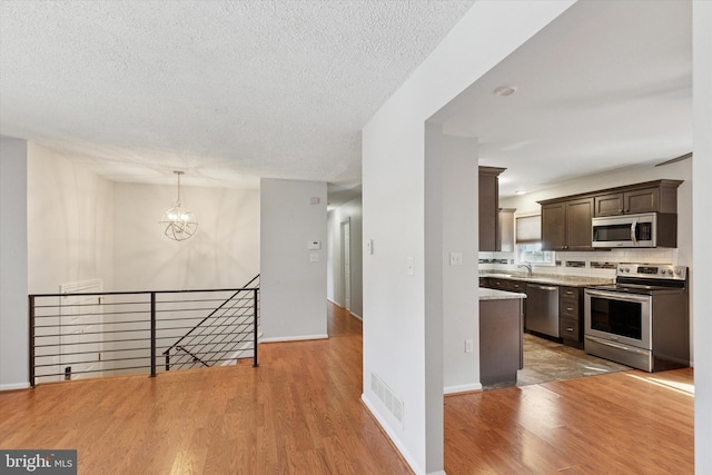 kitchen featuring stainless steel appliances, tasteful backsplash, dark brown cabinetry, wood finished floors, and a chandelier