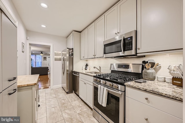 kitchen with sink, backsplash, stainless steel appliances, light stone counters, and white cabinets