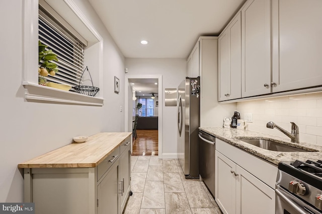 kitchen with appliances with stainless steel finishes, butcher block counters, sink, and decorative backsplash