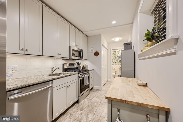 kitchen with stainless steel appliances, tasteful backsplash, sink, and wooden counters