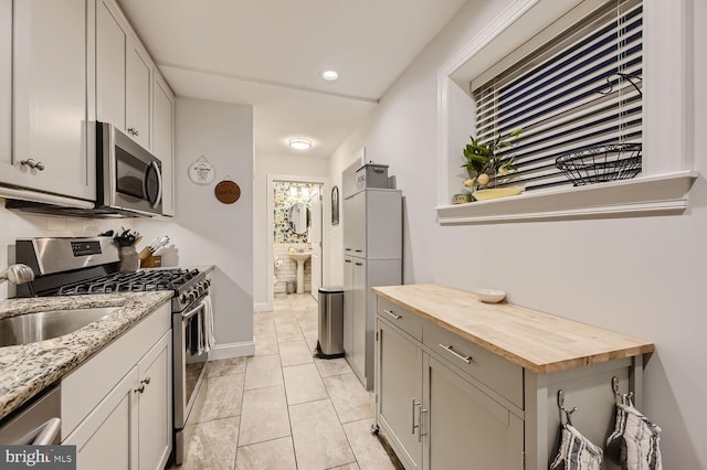 kitchen featuring appliances with stainless steel finishes, butcher block counters, sink, decorative backsplash, and light tile patterned floors