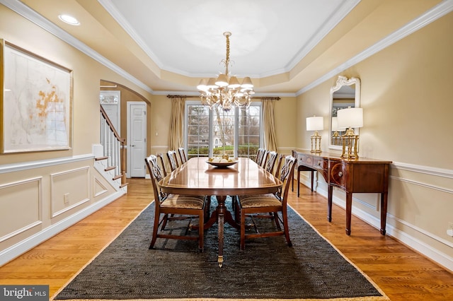 dining room with arched walkways, a raised ceiling, wainscoting, wood finished floors, and an inviting chandelier