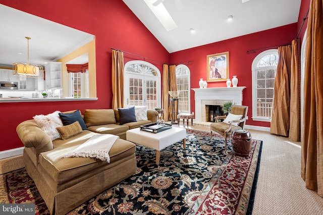 living area with a skylight, high vaulted ceiling, a brick fireplace, and carpet flooring