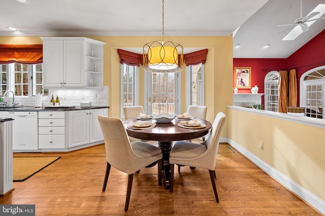 dining room with light wood-style floors, vaulted ceiling, crown molding, and baseboards