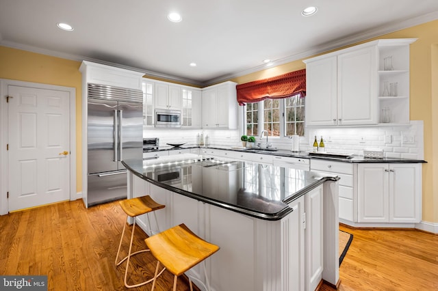 kitchen featuring white cabinets, dark countertops, built in appliances, crown molding, and a sink