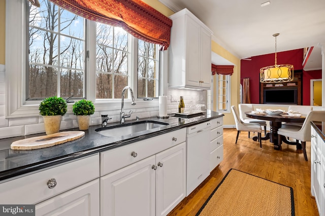 kitchen with dark countertops, light wood finished floors, white dishwasher, and a sink