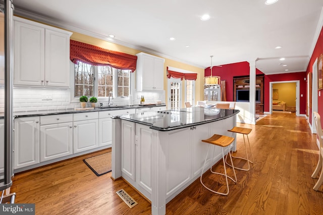 kitchen with a sink, white cabinetry, light wood-style floors, a center island, and dark countertops