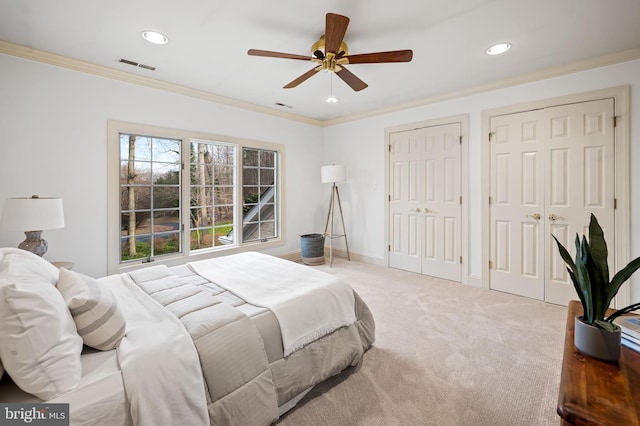 carpeted bedroom featuring recessed lighting, visible vents, baseboards, two closets, and crown molding