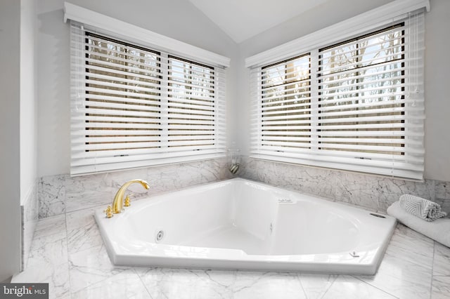 bathroom with lofted ceiling, a garden tub, and marble finish floor