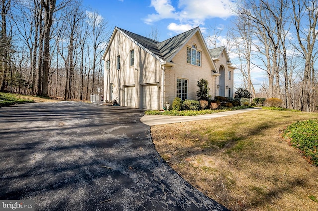 view of side of property featuring aphalt driveway, a lawn, an attached garage, and stucco siding