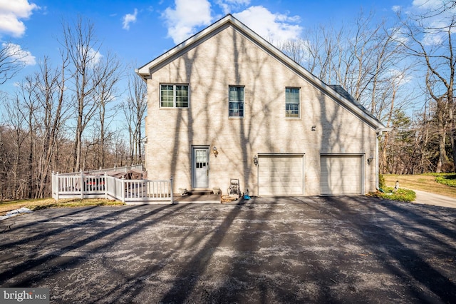 exterior space with an attached garage, a wooden deck, aphalt driveway, and brick siding