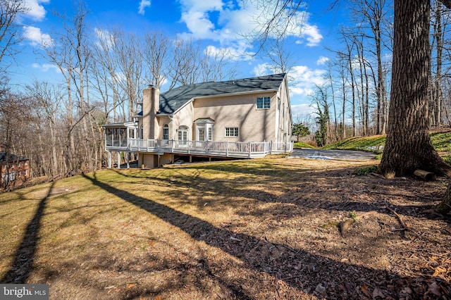 back of property with a chimney, a deck, and a lawn