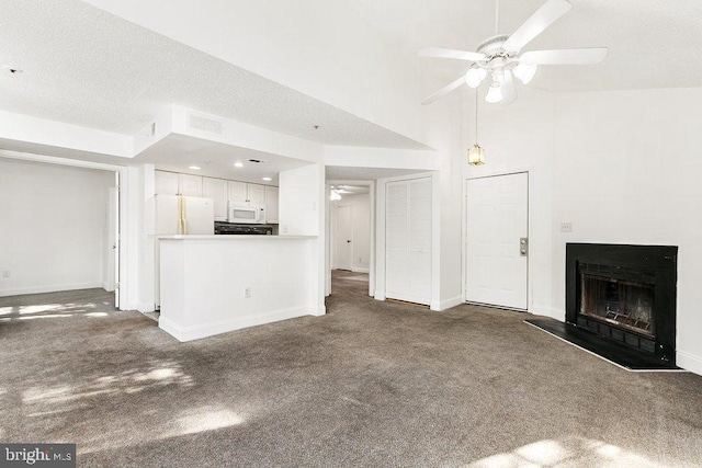 unfurnished living room with a fireplace, a towering ceiling, a ceiling fan, baseboards, and dark colored carpet