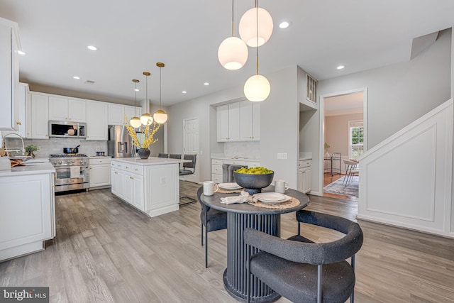 kitchen featuring white cabinetry, hanging light fixtures, stainless steel appliances, a kitchen island, and decorative backsplash